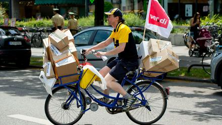 Ein Mitarbeiter der Deutschen Post fährt in München mit einem symbolisch überladenen Postfahrrad über die Straße.