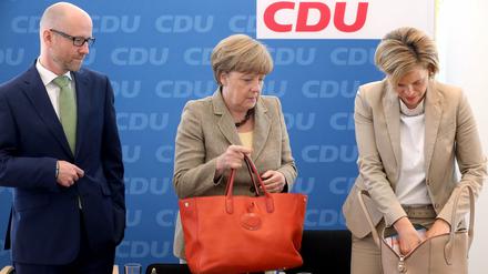 Bundeskanzlerin Angela Merkel und die Fraktionsvorsitzende der CDU im Landtag Rheinland-Pfalz, Julia Klöckner (r), hantieren am 15.06.2015, zu Beginn der Sitzung des Parteivorstands der CDU in Berlin, in ihren Handtaschen. Links schaut der Generalsekretär der Partei, Peter Tauber, interessiert zu. 