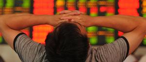 Ein chinesischer Investor vor einer Kurswand schlägt die Hände über dem Kopf zusammen.