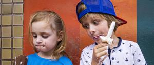 Cute siblings eating popsicles while standing against wall model released Symbolfoto JLOF00414 
