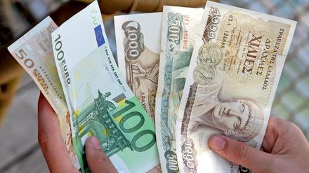 Ein Mann hält zwei Euro-Banknoten (Nennwert 50 und 100 Euro) und drei Drachme-Banknoten in den Händen (1000 und 500 Drachme).