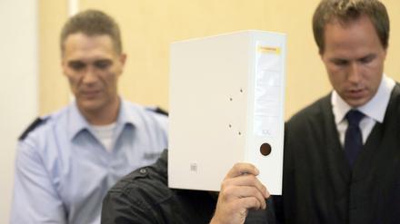 Mit einem Aktenordner vor dem Gesicht kommt am 21.07.2015 in Köln (Nordrhein-Westfalen) ein Angeklagter neben seinem Anwalt Ingmar Rosentreter (r) in den Gerichtssaal. Der Mordprozess gegen einen Mann, der einen anderen wegen eines Streits um eine Pizza erstochen haben soll, hat vor dem Landgericht begonnen.