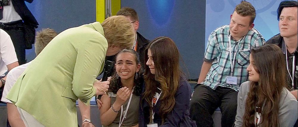 Bundeskanzlerin Angela Merkel (CDU) beugt sich am 15.07.2015 während der Veranstaltung in der von der Regierung gestarteten Gesprächsreihe "Gut leben in Deutschland" in Rostock zu einem Flüchtlingsmädchen palästinensischer Abstammung. Merkels Begegnung mit dem Kind hat in Sozialen Netzwerken zu Kritik geführt.