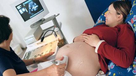 Der Bauch einer Schwangeren wird mit Ultraschall unetrsucht. Die Umrisse des Kindes sind auf dem Bildschirm an der Wand zu erkennen.