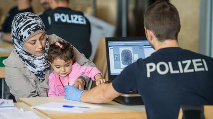 Ein Beamter der Bundespolizei nimmt am 14.07.2015 im Notquartier der Bundespolizeiinspektion in Passau (Bayern) mit einem Scanner Fingerabdrücke von der syrischen Flüchtlingsfrau Delal mit ihrer Tochter. Die Zahl illegaler Einreisen nach Deutschland steigt rasant und stellt die Bundespolizei vor wachsende Probleme. 