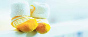 Symbol des Verlusts. Zwei gelbe Babyschuhe auf dem Schutzgitter eines Kinderbetts.