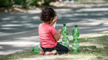 Ein Flüchtlingskind sitzt am 06.08.2015 in Berlin auf dem Gelände des Landesamtes für Gesundheit und Soziales (LaGeSo) auf einem Grünstreifen. 