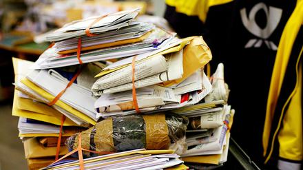 Stapel Post mit Postbote schemenhaft im Hintergrund.