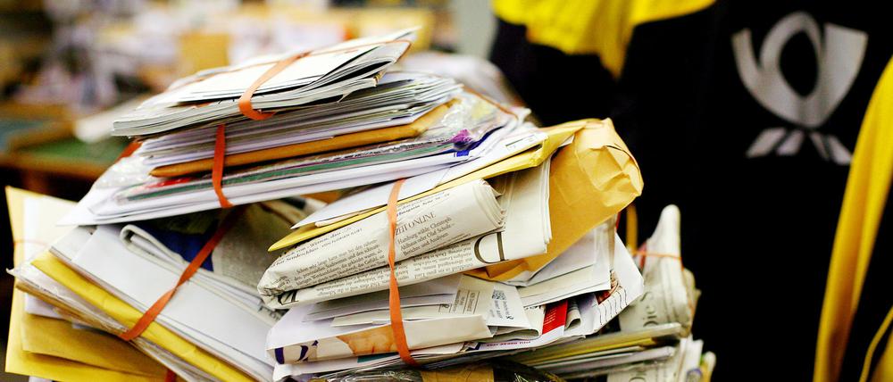 Stapel Post mit Postbote schemenhaft im Hintergrund.
