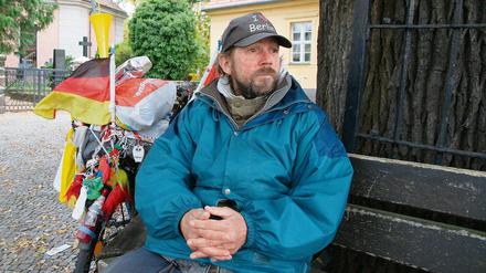 Peter, ein wohnungsloser Zehlendorfer; in seinem "Wohnzimmer" vor der Dorfkirche, der Friedenseiche und der alten Dorfschule in Zehlendorf-Mitte.