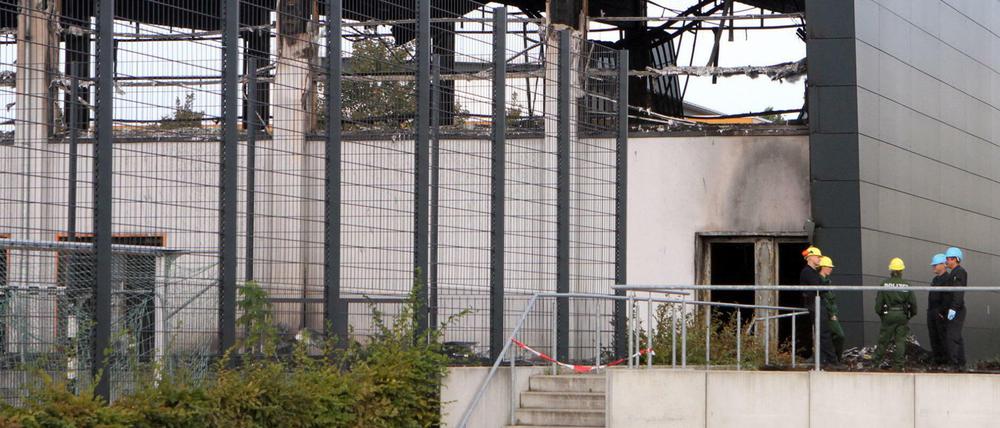 Aufgebrochen und angezündet: Die abgebrannte Halle in Nauen, rechts davor die Ermittler der Polizei.
