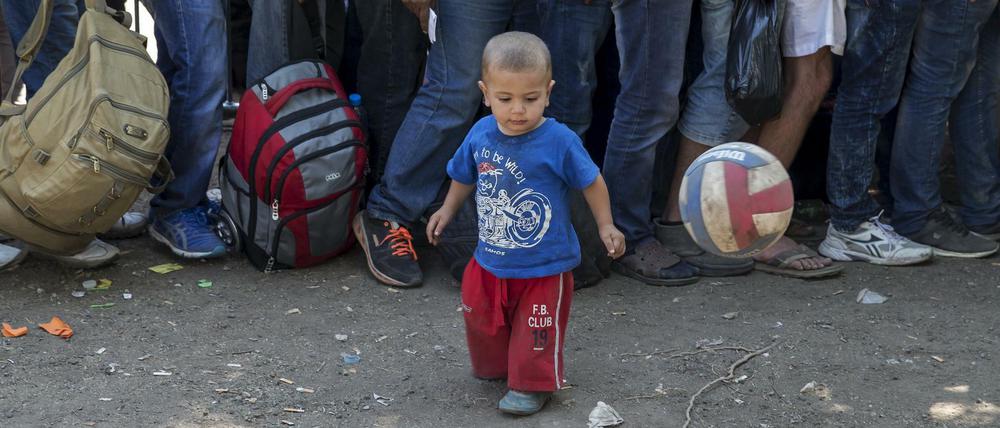 Flüchtlinge stehen in Serbien Schlange, während ein Kind mit dem Ball spielt.