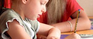 Ein Kind im Grundschulalter sitzt vor Mathe-Aufgaben, eine Frau schaut ihm dabei zu.