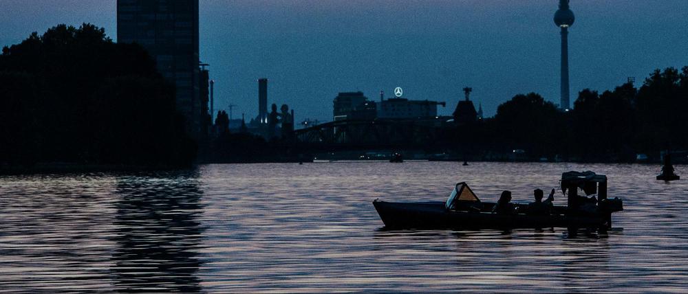 Ein Motorboot fährt abends auf der Spree. Im Hintergrund sind Allianz-Tower und der Fernsehturm zu sehen.