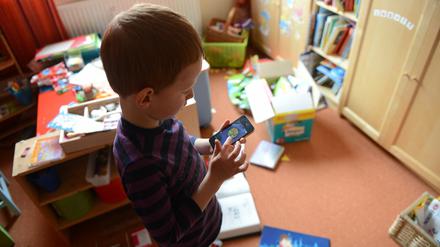 Ein Junge spielt in seinem Kinderzimmer auf einem Smartphone ein Computerspiel.