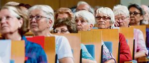 In einem Hörsaal sitzen ältere Frauen und Männer und blicken nach vorne.
