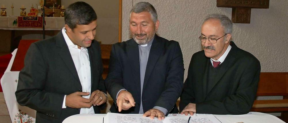 SPD-Fraktionschef Raed Saled beugt sich mit Abuna Murat Üzel und Amill Gorgis von der Syrisch-Orthodoxen Kirche über aramäische Gebetsbücher.