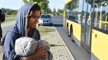Eine Frau aus Sri Lanka geht am 08.09.2015 am Bahnhof in Schönefeld (Brandenburg) mit ihrem Kind zu einem bereit stehenden Bus. Mit einem Zug aus München kamen 450 Flüchtlinge, die in verschiedenen Notunterkünften in Berlin untergebracht werden. 