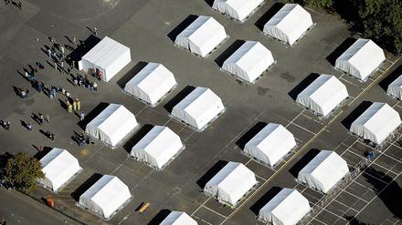 Flüchtlinge stehen am 09.09.2015 zwischen exakt ausgerichteten Zelten in der ehemaligen Schmidt-Knobelsdorf-Kaserne der Polizei in Berlin-Spandau vor einem Container der Senatsverwaltung. In den letzten Tagen sind hier über 300 Kriegsflüchtlinge angekommen, etwa 600 Flüchtlinge können untergebracht werden. 