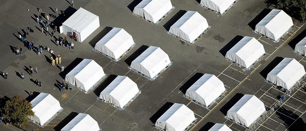 Flüchtlinge stehen am 09.09.2015 zwischen exakt ausgerichteten Zelten in der ehemaligen Schmidt-Knobelsdorf-Kaserne der Polizei in Berlin-Spandau vor einem Container der Senatsverwaltung. In den letzten Tagen sind hier über 300 Kriegsflüchtlinge angekommen, etwa 600 Flüchtlinge können untergebracht werden.
