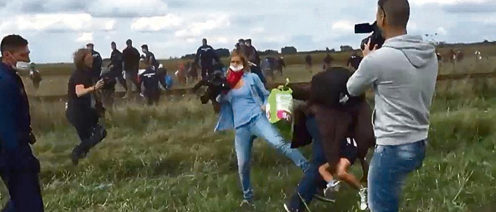 Eine Kamerafrau des ungarischen Senders N1TV stellt in Röszke einem Flüchtling, der ein kleines Kind auf dem Arm trägt, ein Bein.