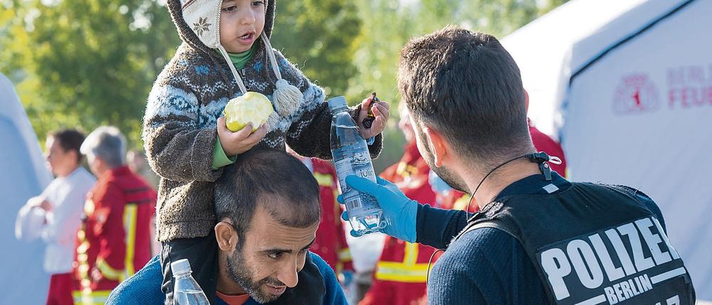 Ein Berliner Polizist verteilt Wasserflaschen an einen Vater aus Syrien und sein Kind, die zuvor mit weiteren Flüchtlingen am Bahnhof in Schönefeld (Brandenburg) angekommen waren.