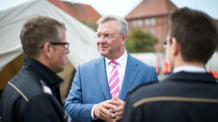 ARCHIV - Frank Henkel (M, CDU), Berliner Innensenator, unterhält sich am 03.09.2015 auf dem Gelände der ehemaligen Schmidt-Knobelsdorf-Kaserne der Polizei in Berlin-Spandau mit Feuerwehrleuten über die Situation in der Flüchtlingsunterkunft. 