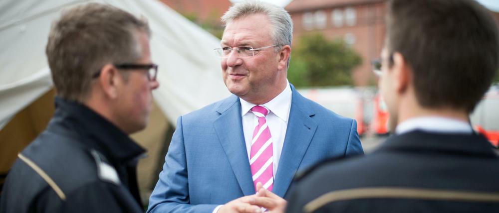 ARCHIV - Frank Henkel (M, CDU), Berliner Innensenator, unterhält sich am 03.09.2015 auf dem Gelände der ehemaligen Schmidt-Knobelsdorf-Kaserne der Polizei in Berlin-Spandau mit Feuerwehrleuten über die Situation in der Flüchtlingsunterkunft.