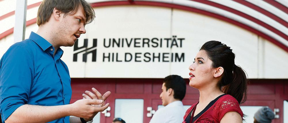 Ein Juniorprofessor und eine Studentin stehen vor der Universität Hildesheim und sprechen miteinander.