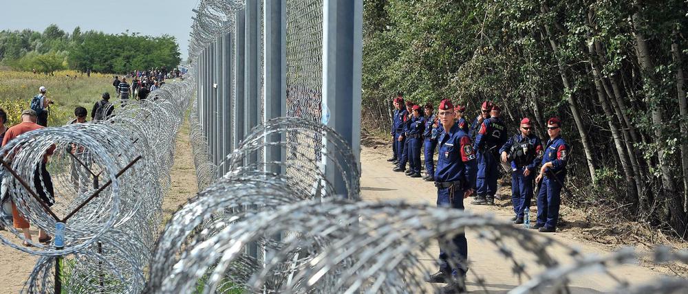 Hüben und drüben. Flüchtlinge laufen nahe der nordserbischen Stadt Horgos auf serbischer Seite an der mit Stacheldraht gesicherten Grenze entlang, an der auf ungarischer Seite Polizisten aufmarschiert sind. 
