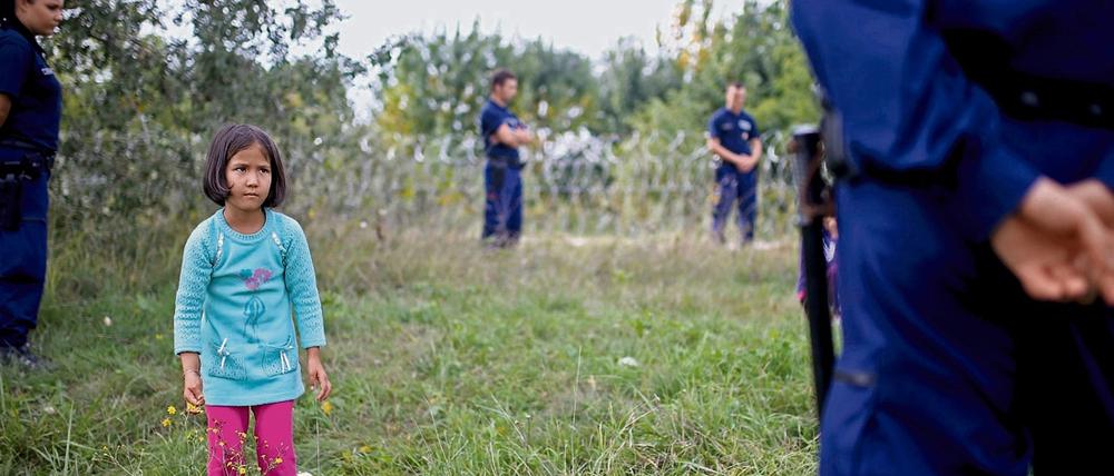 Ein Mädchen steht zwischen ungarischen Grenzbeamten, die es wegen illegalen Grenzübertritts festhalten.