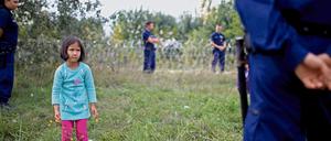 Ein Mädchen steht zwischen ungarischen Grenzbeamten, die es wegen illegalen Grenzübertritts festhalten.