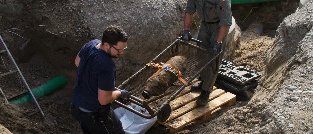 Zwei Kampfmittelräumer wuchten die 50-Kilo-Bombe nach der Entschärfung aus der Baugrube.