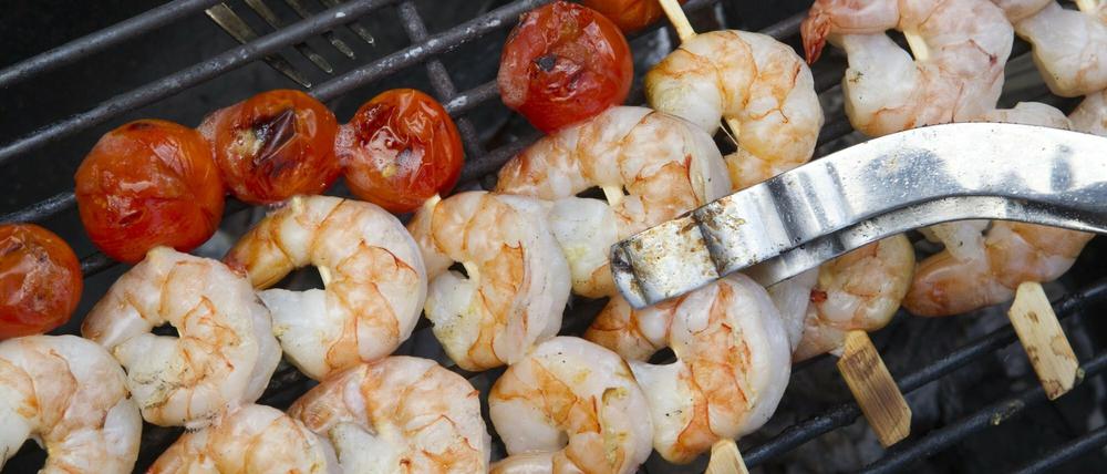 Scampi und Cocktail-Tomaten liegen beim Barbeque auf einem Grill.