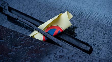 Ein Strafzettel (Knöllchen) steckt in einem Scheibenwischer eines geparkten Autos.