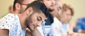 Männer und Frauen sitzen an einem Tisch und schreiben in ihre Hefte.