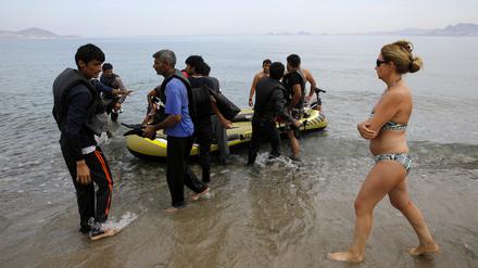 Eine spanische Touristin läuft vorbei, als Flüchtlinge aus Pakistan am Strand der griechischen Insel Kos ankommen.