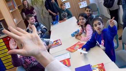 Schulkinder sitzen an einem Tisch und melden sich.