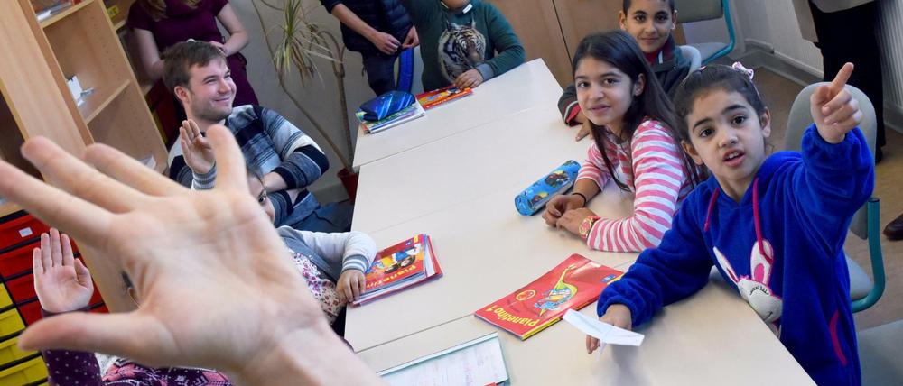 Schulkinder sitzen an einem Tisch und melden sich.