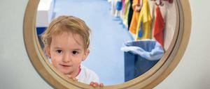 Ein Kleinkind schaut aus einem Fenster in einer Tür heraus.