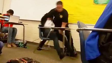 Festnahme im Klassenraum. Ein Polizist reißt eine Schülerin vom Stuhl.