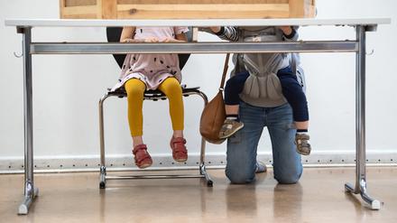 Eine junge Mutter mit zwei Kinder kniet hinter der Wahlkabine in der Jane-Addams-Schule in Friedrichshain und füllt ihre Stimmzettel aus. +++ dpa-Bildfunk +++