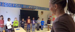 In einem Klassenraum steht eine Lehrerin vor einer Gruppe von Schülern.