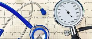 Risikofaktor Bluthochdruck. Eine Blutdruckmanschette und ein Stethoskop auf dem Ausdruck einer Herzstromkurve, einem Elektrokardiogramm (EKG).