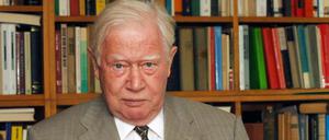 Hans Mommsen sitzt vor einem Bücherregal und blättert in einem Buch.