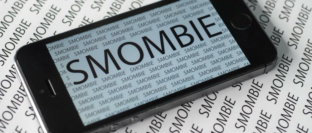 Das Wort "Smombie" ist am 13.11.2015 in München (Bayern) vielfach auf einem Smartphone und auf einem Zettel zu sehen. Der Langenscheidt-Verlag hat "Smombie" zum "Jugendwort des Jahres" gekürt. Es ist zusammengesetzt aus den Worten Smartphone und Zombie und beschreibt jemanden, der von seiner Umwelt nichts mehr mitbekommt, weil er nur noch auf sein Smartphone starrt.