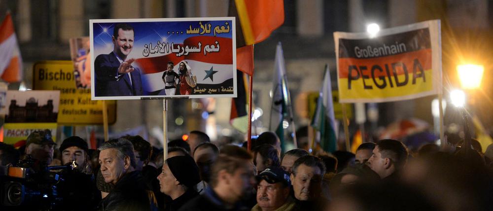 Pegida-Demonstration am 9. November in Dresden: Anhänger halten ein Plakat mit dem Antlitz des syrischen Präsidenten Baschar al-Assad hoch, auf dem in arabischer Schrift steht: "Wir sagen Ja zu Assad, Ja zu einem Syrien, das sicher ist".