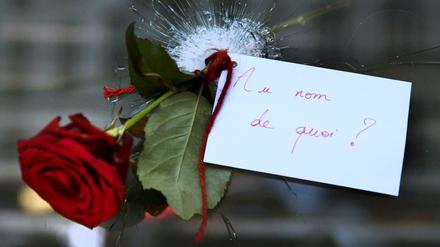 Eine Rose, durch ein Einschussloch einer Scheibe gesteckt in Paris. Auf dem Zettel steht: "Im Namen von was?"