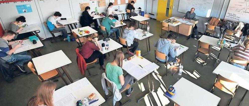 Schüler sitzen in einem Klassenraum an Einzeltischen vor Aufgabenblättern.