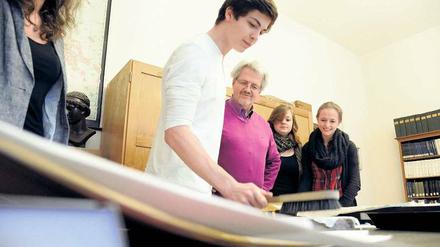 Ein Schüler schlägt mit einer Bürste auf ein Papier, das auf einer Steintafel liegt.